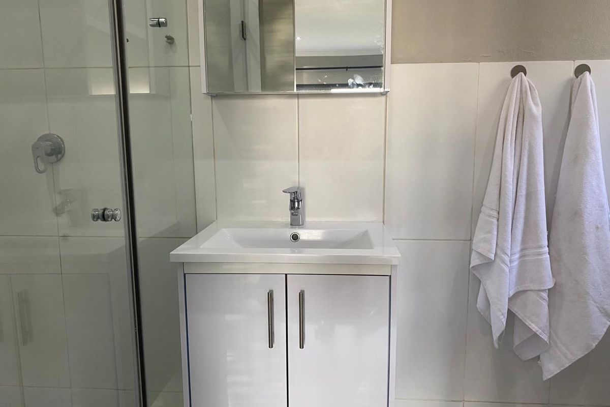 A clean, modern bathroom featuring a white vanity cabinet with a basin, a wall-mounted mirror cabinet, and a glass-enclosed shower area.