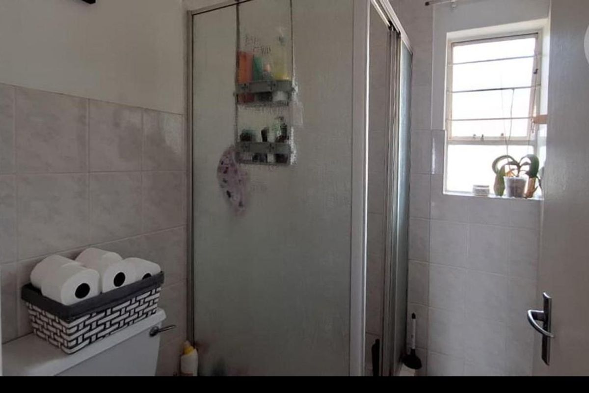 A functional bathroom featuring a corner shower enclosure, tiled walls, and a window for natural light.
