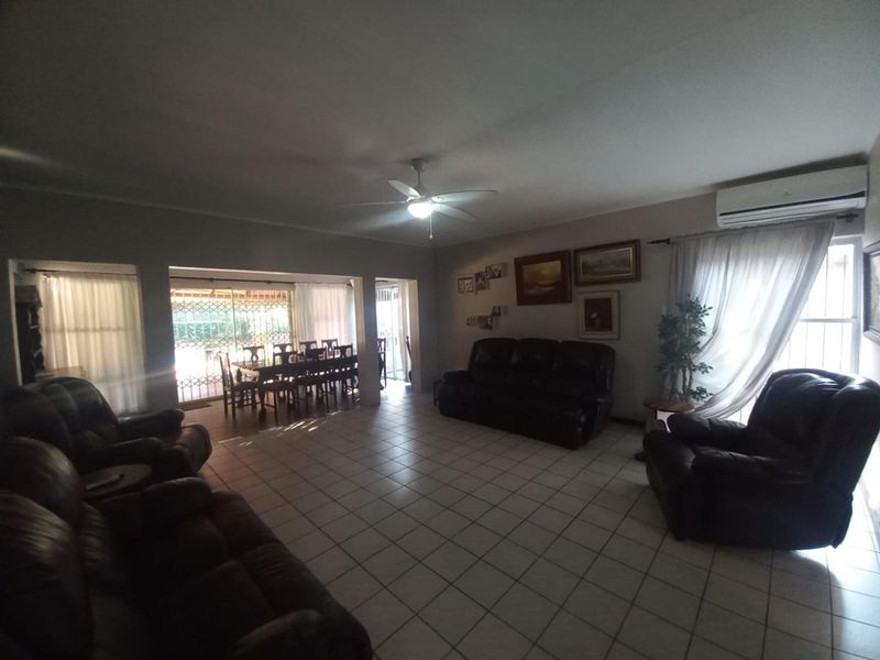 Spacious open-plan living and dining area featuring tiled flooring, a ceiling fan, and a wall-mounted air conditioning unit.