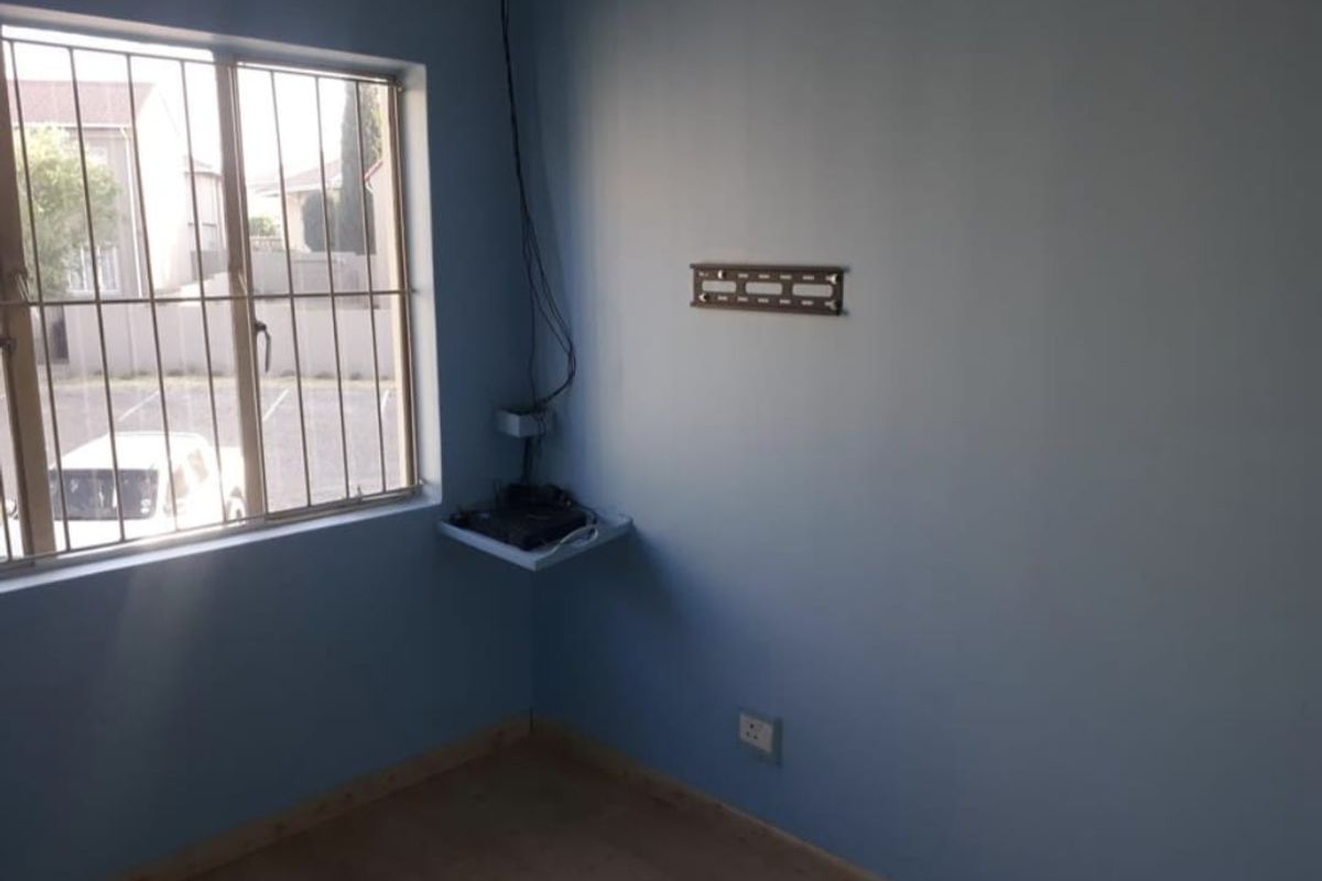 A bedroom featuring a window with security bars, a wall-mounted television bracket, and a small corner shelf with electrical points.