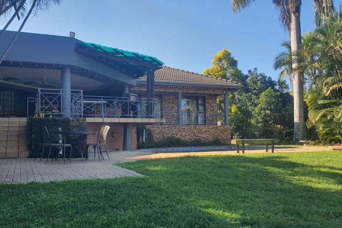 Rear view of the property featuring a raised patio area, swimming pool, and established garden surroundings.