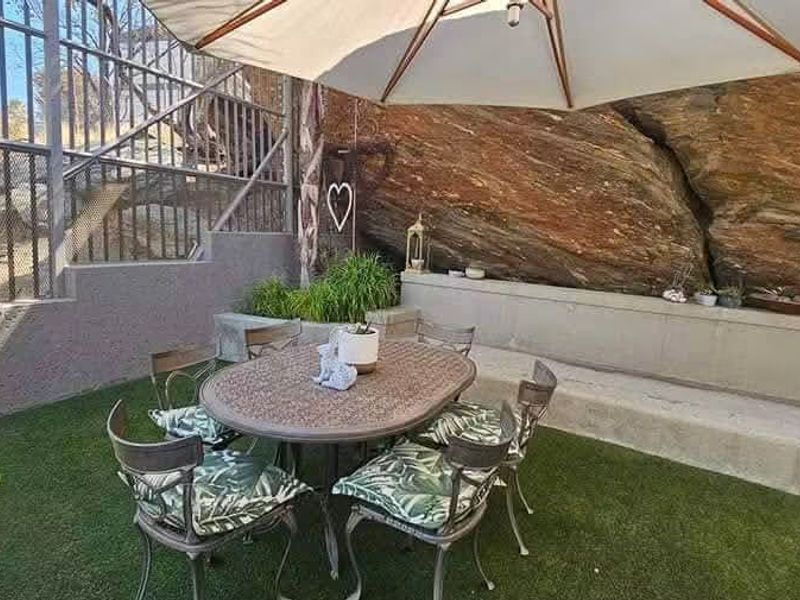 A unique outdoor patio area featuring a natural rock face backdrop, built-in concrete bench seating, and artificial turf flooring.