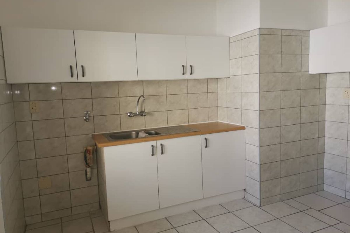 A functional kitchen area featuring white cabinetry, a stainless steel sink, and tiled walls and flooring throughout.