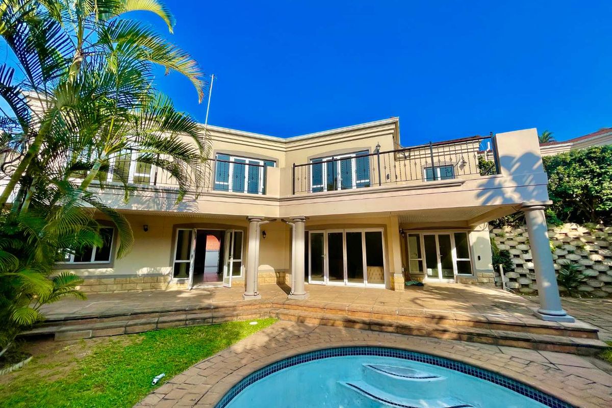 Rear view of the townhouse featuring a spacious covered patio, swimming pool, and a balcony with wrought iron railings overlooking the garden.