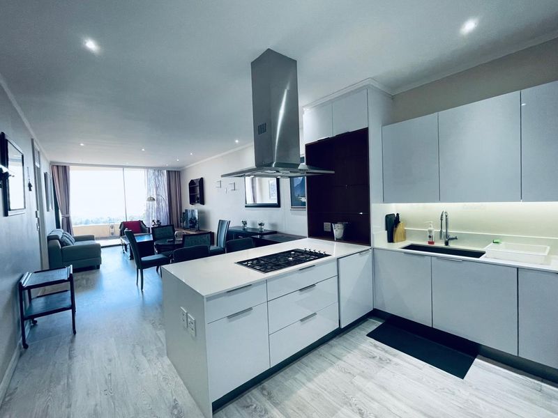 Modern open-plan kitchen featuring a central island with gas hob, sleek cabinetry, and integrated extractor, flowing into a bright living and dining area.