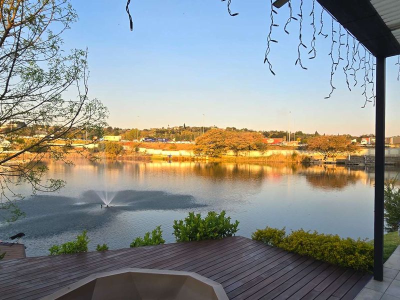 A spacious covered patio featuring timber decking and tiled flooring, offering scenic views over a tranquil lake with a central fountain.