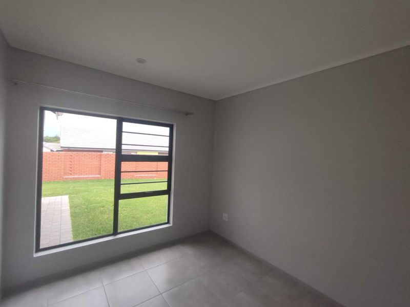 A clean, empty bedroom featuring neutral grey walls, tiled flooring, and a large window overlooking the garden.