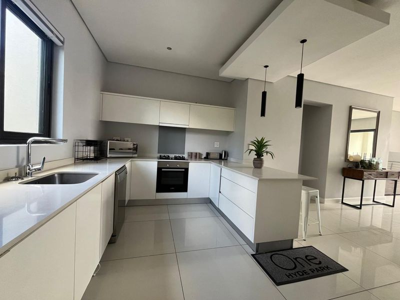 Modern kitchen featuring sleek white cabinetry, stone countertops, integrated appliances, and a functional layout with a breakfast bar and contemporary pendant lighting.