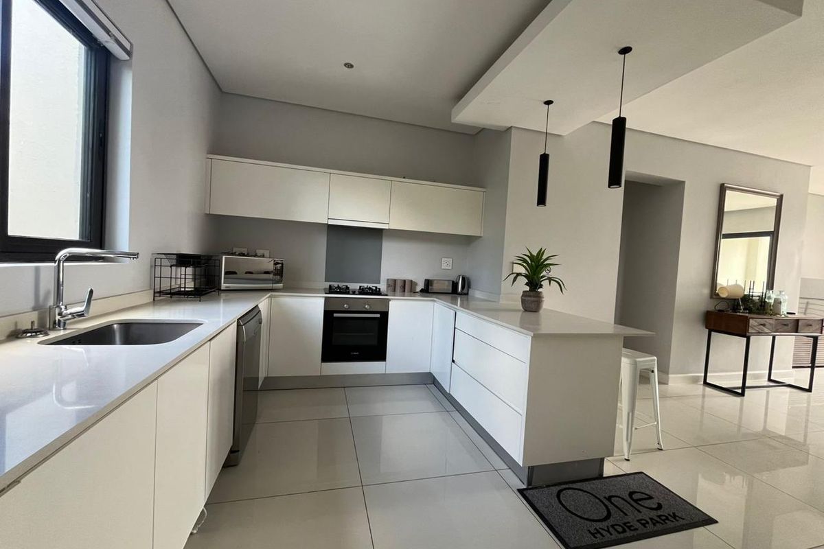 Modern kitchen featuring sleek white cabinetry, stone countertops, integrated appliances, and a functional layout with a breakfast bar and contemporary pendant lighting.