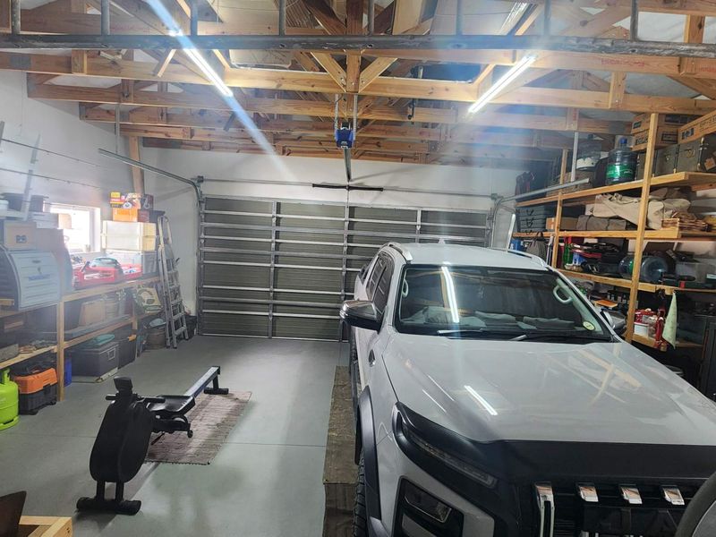 A spacious garage featuring exposed timber roof trusses, concrete flooring, and extensive built-in timber shelving for storage.