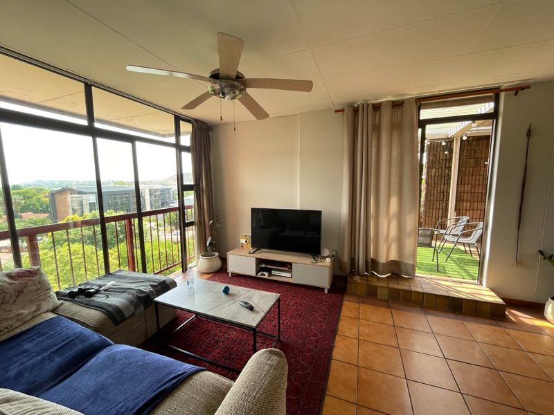 Spacious living room featuring tiled floors, a ceiling fan, and large glass doors providing natural light and direct access to an outdoor balcony area.