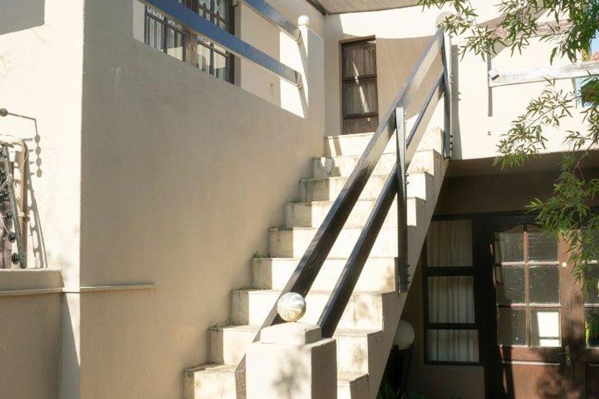 Exterior view of an apartment building featuring an external staircase leading to an upper-level balcony and a ground-floor entrance.