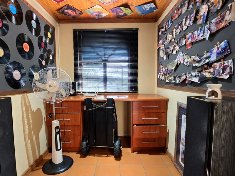 A dedicated home office space featuring a built-in desk, timber ceiling, and tiled flooring, currently styled as a music-themed hobby room.