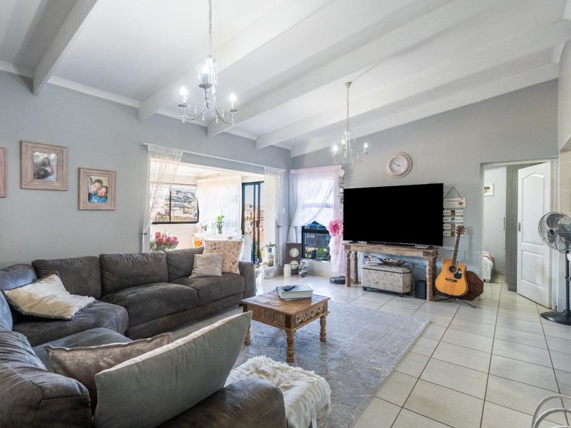 Spacious living room featuring high exposed beam ceilings, neutral tiled flooring, and elegant chandelier lighting, creating a bright and inviting atmosphere.