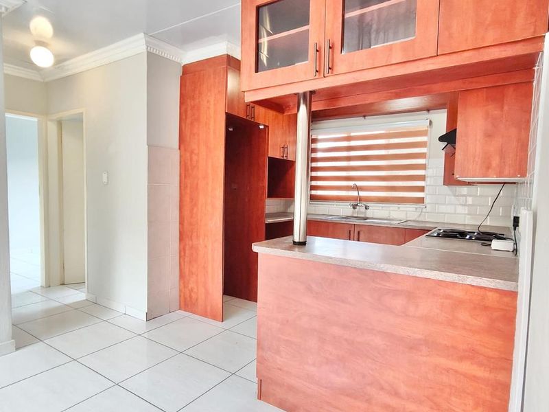 A functional kitchen featuring wooden cabinetry, a subway tile backsplash, and a breakfast bar, finished with neutral ceramic floor tiles.