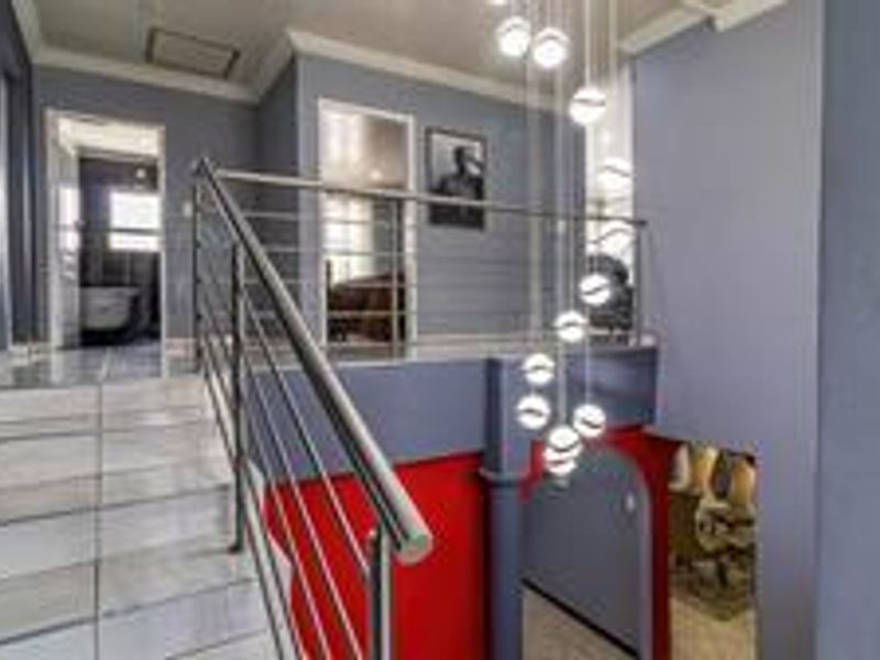 A bright landing area featuring a modern stainless steel balustrade, tiled staircase, and a striking multi-pendant light fixture overlooking the lower level.