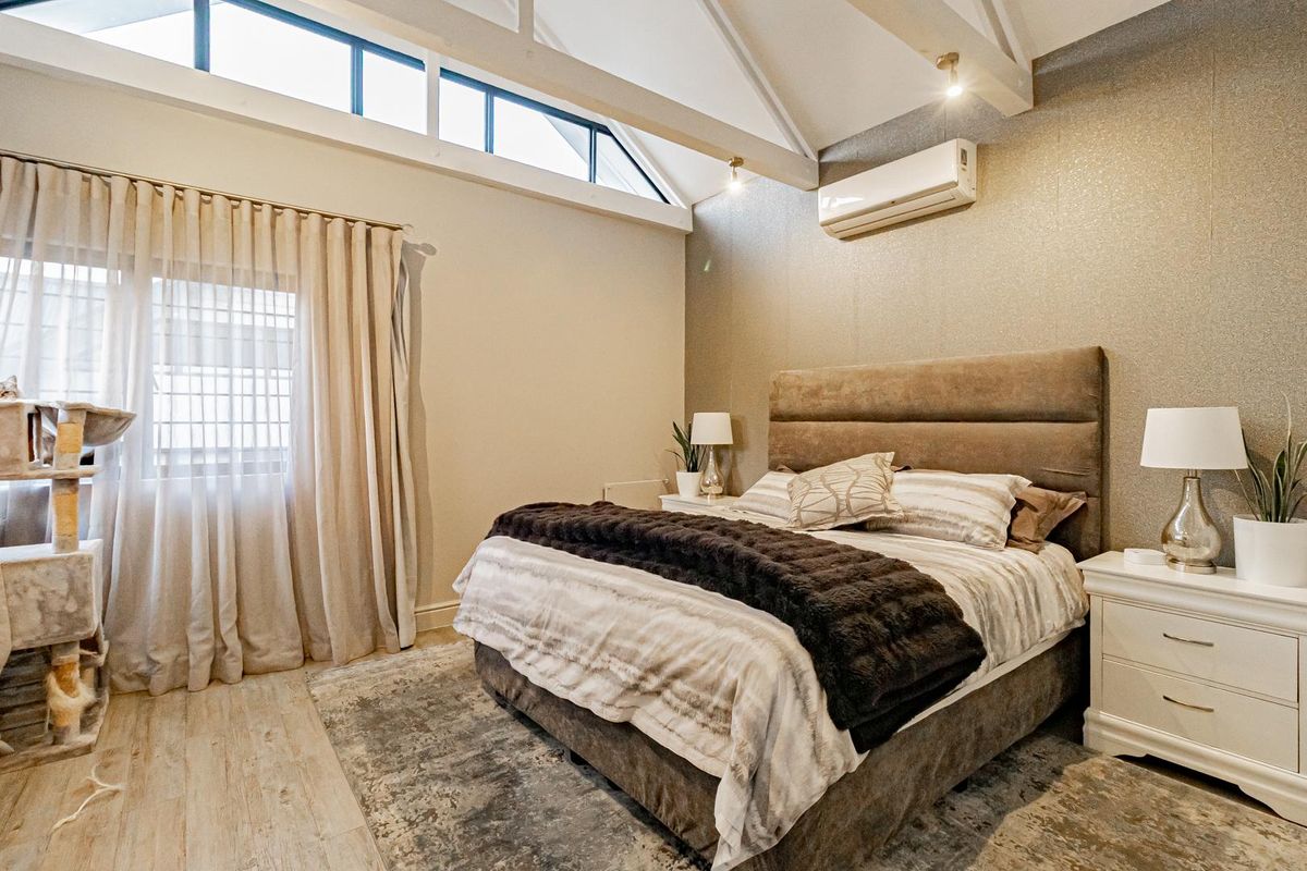 Spacious bedroom featuring high vaulted ceilings with exposed beams, clerestory windows, and a wall-mounted air conditioning unit.