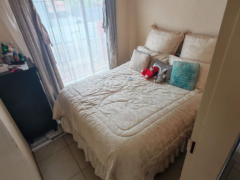 A compact bedroom featuring tiled flooring and a window with security bars, providing a functional and private sleeping space.