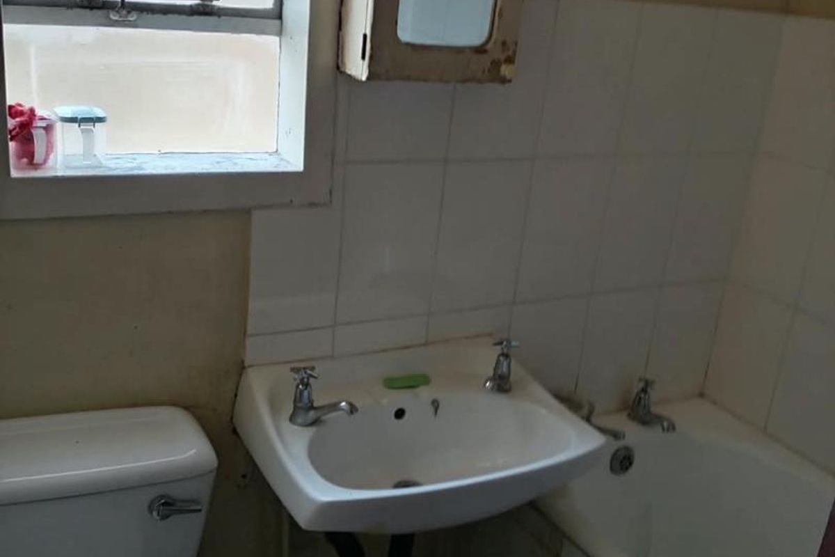 A dated bathroom featuring a wall-mounted basin, bathtub, and toilet, requiring cosmetic updates to improve its overall condition and appeal.