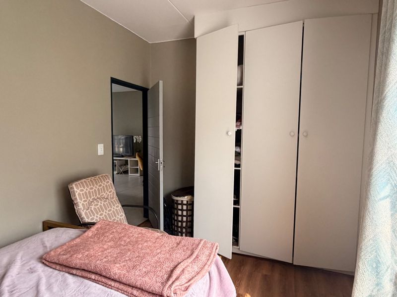 A bedroom featuring laminate flooring and a large built-in wardrobe with white doors, providing ample storage space.