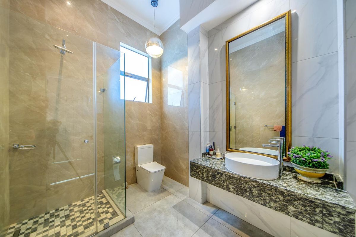 Modern bathroom featuring a glass-enclosed shower, floating granite vanity with vessel sink, and large wall mirror with elegant tile finishes.