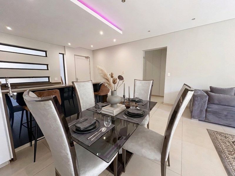Modern open-plan living and dining area featuring sleek tiled floors, recessed ceiling lighting with ambient LED accents, and a functional breakfast bar.