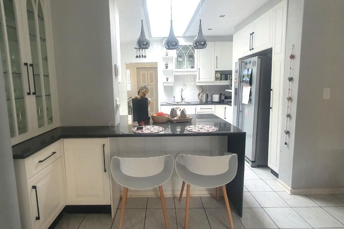 Modern kitchen featuring white cabinetry, granite countertops, a central island with breakfast bar seating, and a skylight providing natural light.
