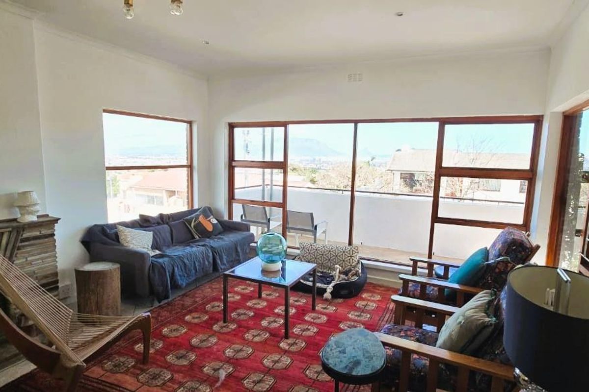 A bright living room featuring a stone fireplace, large timber-framed windows, and sliding doors that open onto an outdoor balcony with scenic views.