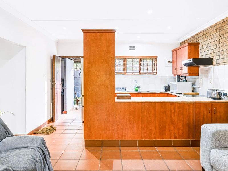 Open plan kitchen featuring wooden cabinetry, tiled flooring, and an exposed brick feature wall, with direct access to an outdoor area.