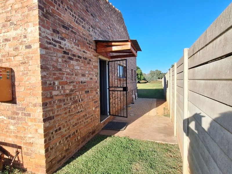 Rear exterior view of the industrial property featuring exposed brickwork, a secure metal entrance gate, and a paved walkway alongside a concrete boundary wall.