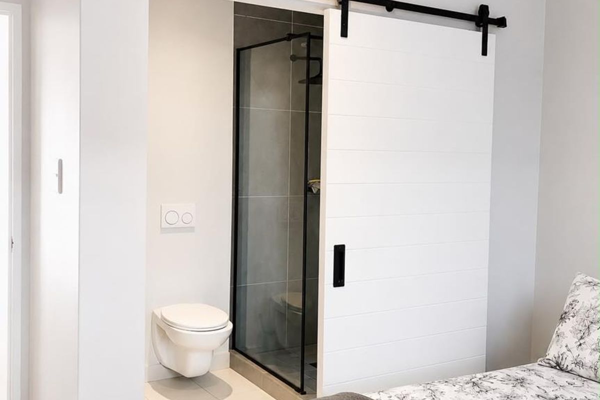 Modern en-suite bathroom featuring a sliding barn door, wall-mounted toilet, and a glass-enclosed shower, seamlessly integrated with the bedroom.