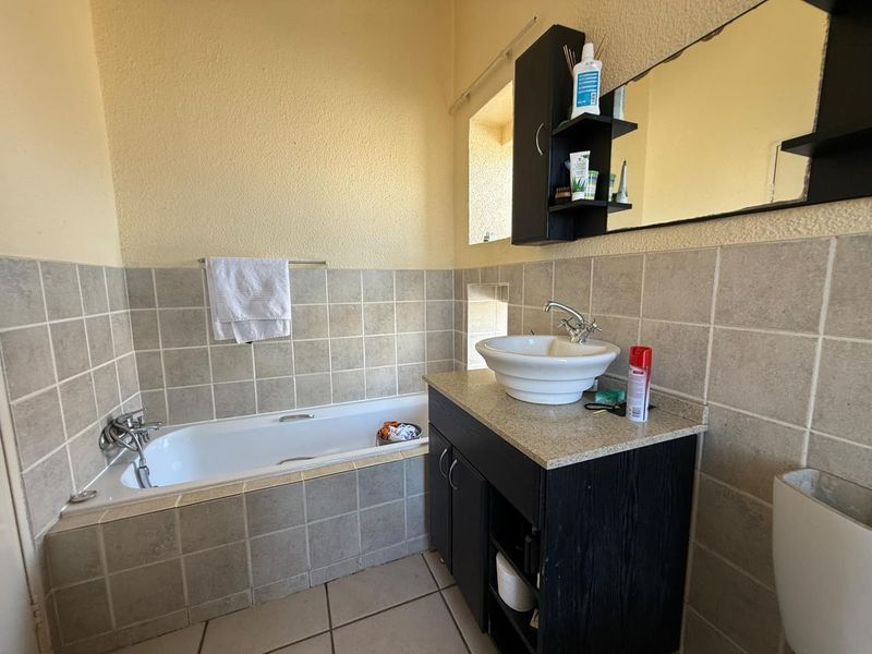 A functional bathroom featuring a built-in bathtub, a vanity cabinet with a vessel sink, and neutral wall tiling.