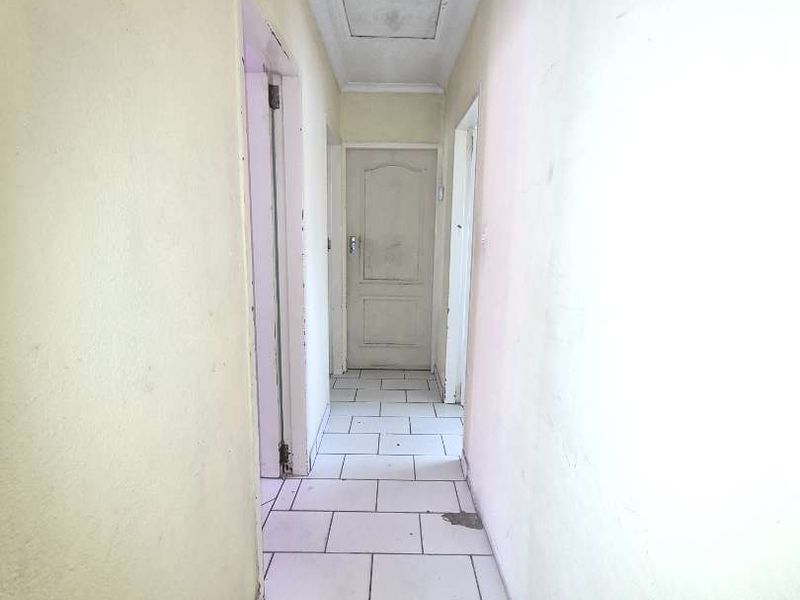 A narrow hallway featuring tiled flooring and a ceiling access hatch, currently in need of cosmetic updates and repairs to the wall finishes.