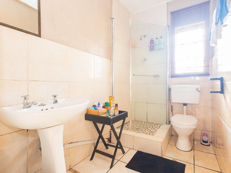 A compact bathroom featuring a pedestal basin, a shower enclosure, and a toilet, finished with neutral wall and floor tiling.