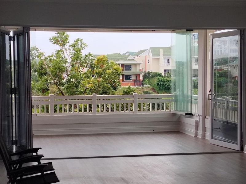A spacious, empty balcony featuring modern stacking glass doors and a protective railing, offering a pleasant view of the surrounding residential area.