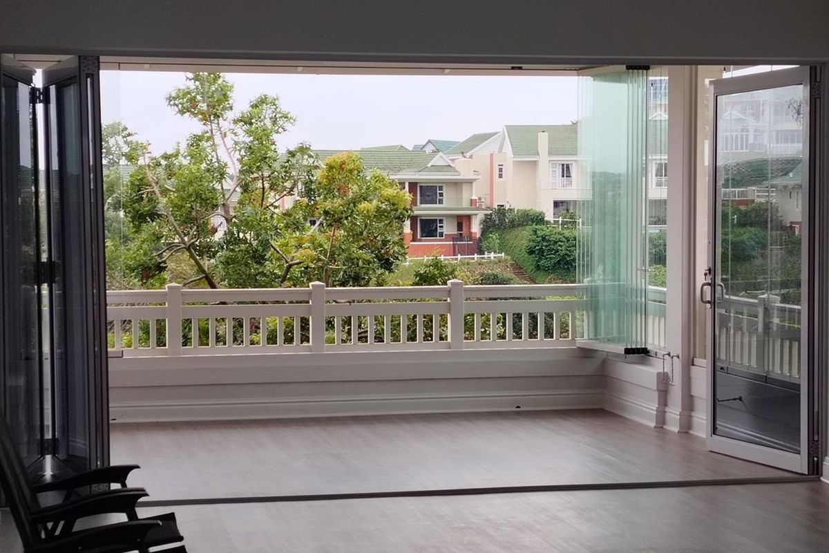 A spacious, empty balcony featuring modern stacking glass doors and a protective railing, offering a pleasant view of the surrounding residential area.