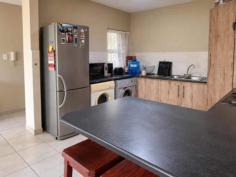 Functional kitchen featuring laminate cabinetry, dark countertops, an electric hob, and tiled flooring, with integrated space for laundry appliances.