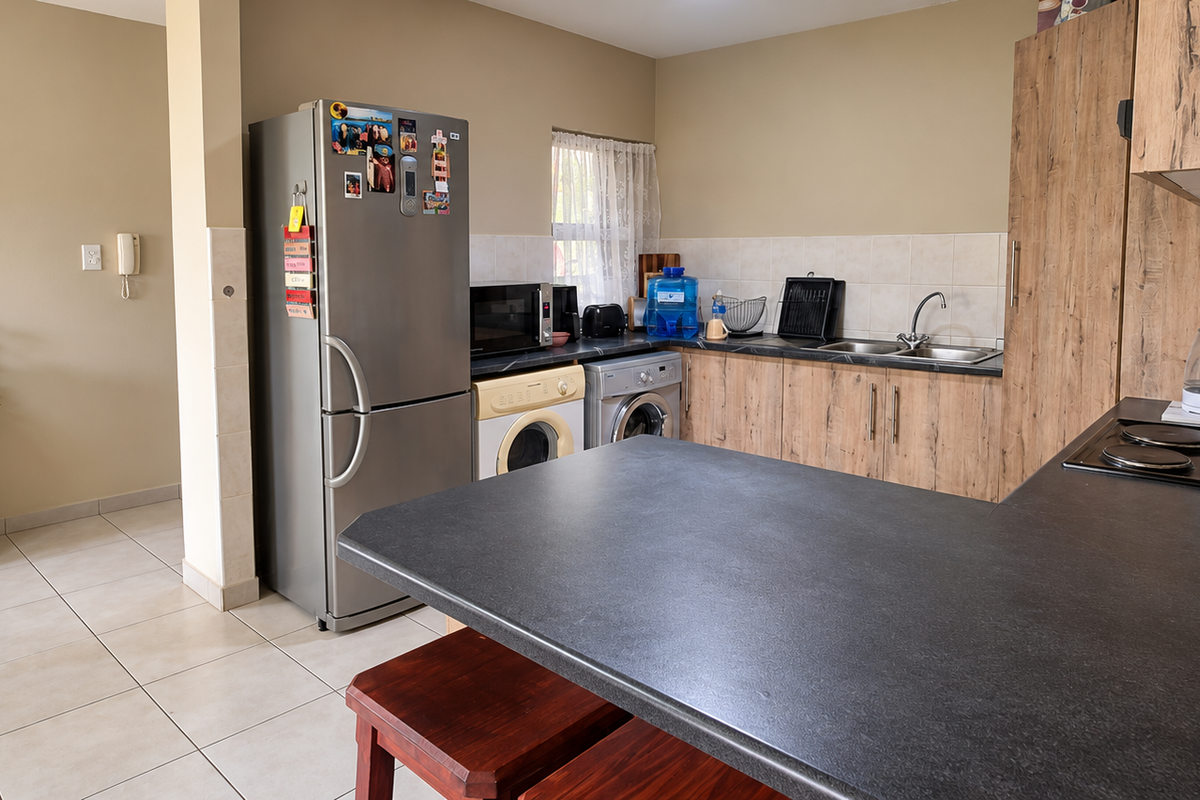 Functional kitchen featuring laminate cabinetry, dark countertops, an electric hob, and tiled flooring, with integrated space for laundry appliances.