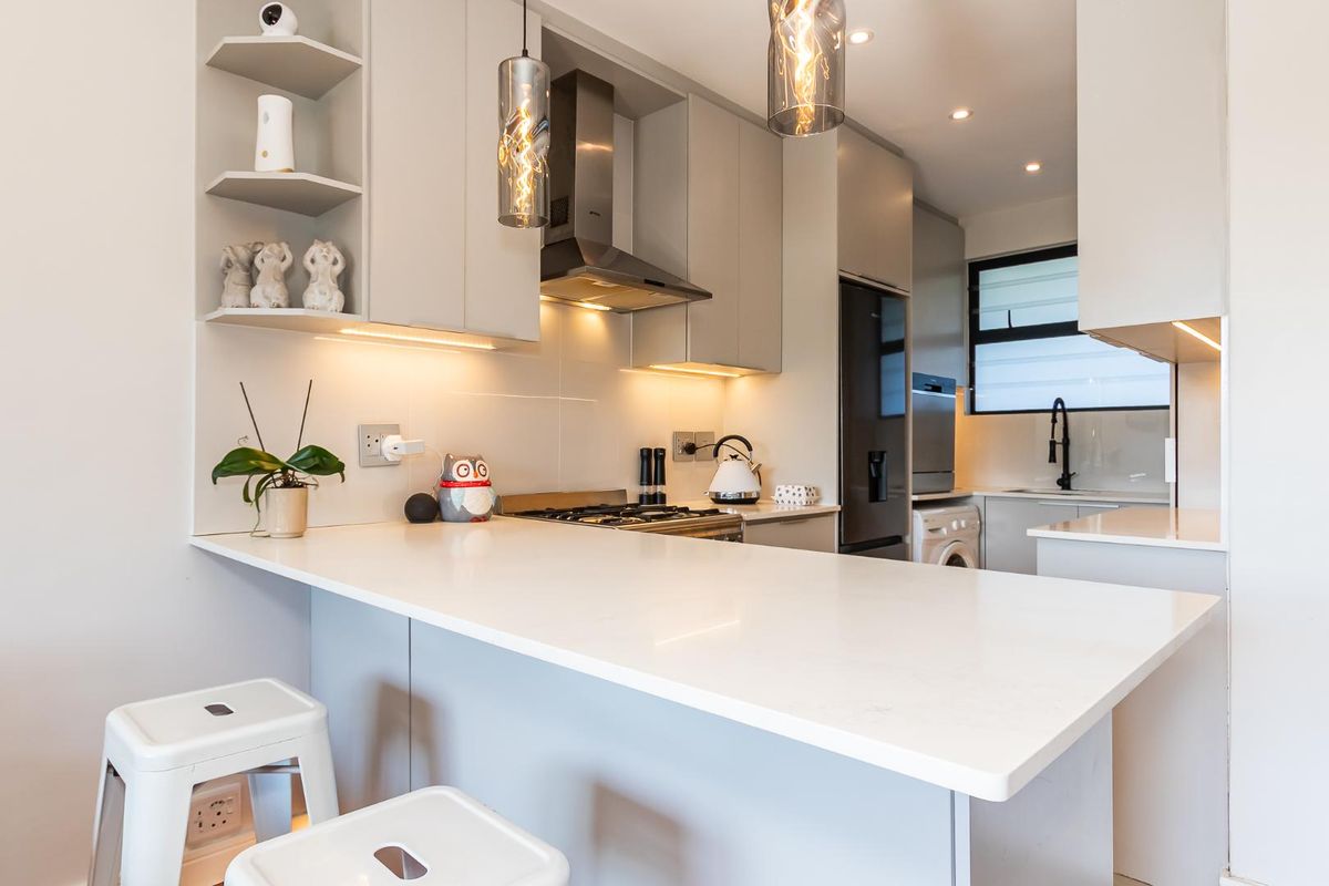 Modern kitchen featuring sleek cabinetry, quartz countertops, a gas hob, extractor fan, and integrated laundry space with contemporary finishes and lighting.