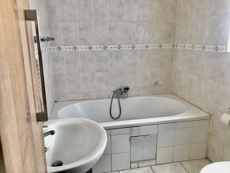 A functional bathroom featuring a built-in bathtub with wall-mounted mixer, pedestal basin, and neutral ceramic wall tiling throughout.