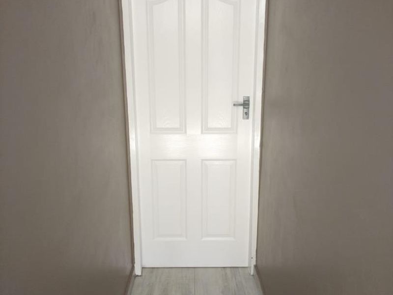 A narrow hallway featuring neutral wall paint and modern wood-look floor tiles leading to an internal door.