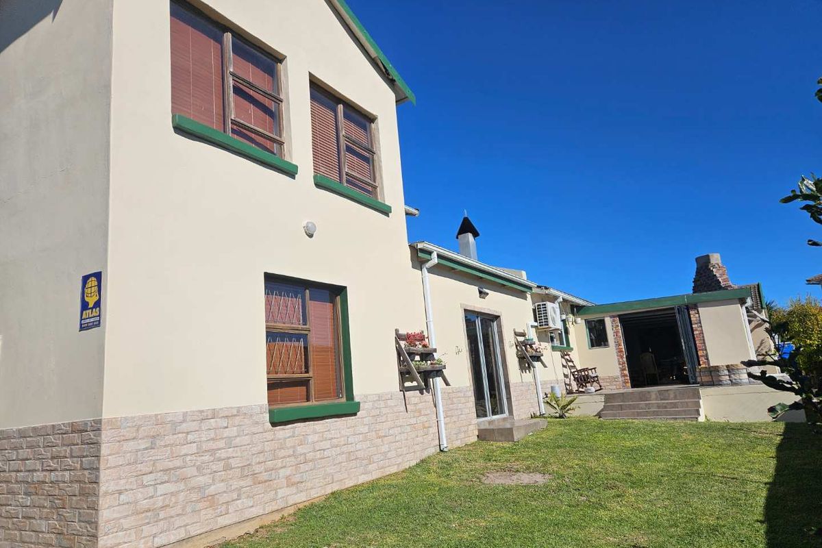 Rear view of the house featuring stone cladding, a well-maintained lawn, sliding glass doors, and an outdoor chimney structure.