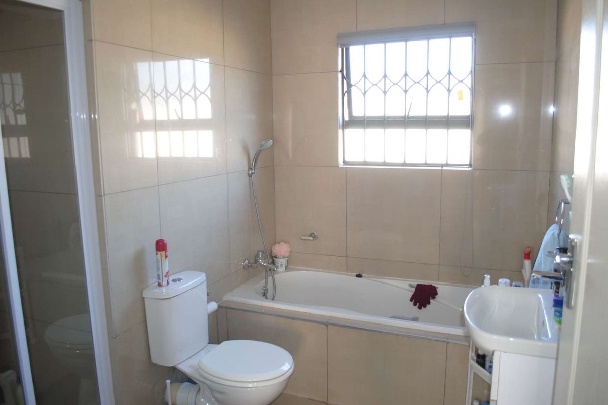 A functional bathroom featuring floor-to-ceiling wall tiles, a built-in bathtub, a separate shower enclosure, a toilet, and a pedestal basin.