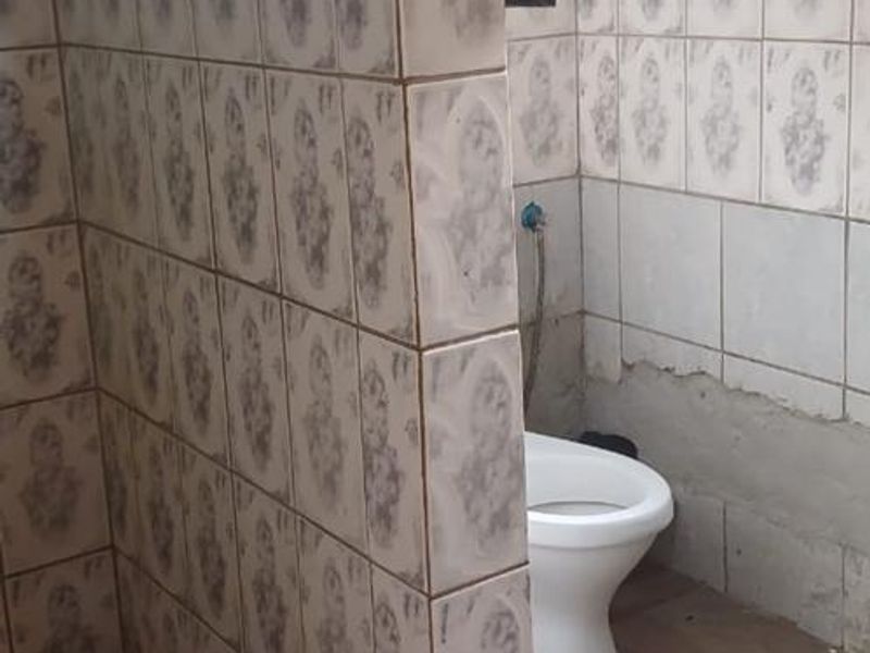 A bathroom featuring a tiled shower enclosure and toilet, currently showing significant wear with missing wall tiles and damaged finishes requiring renovation.