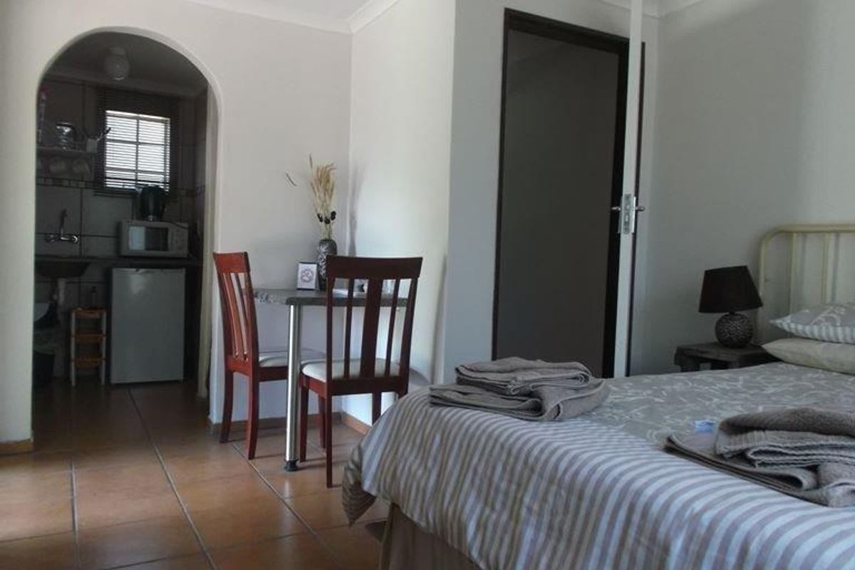 A bedroom featuring tiled flooring and an arched entryway leading to a small kitchenette area.