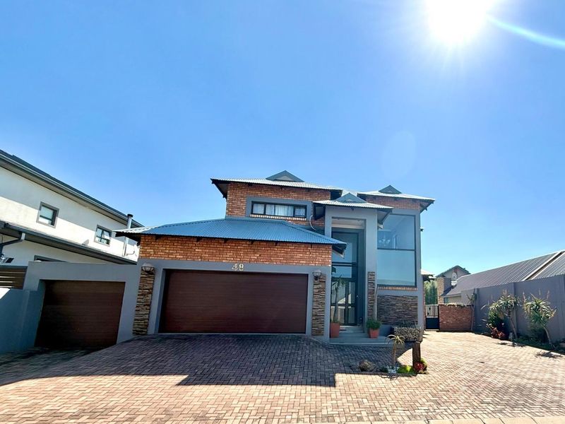 A modern double-story residential home featuring a brick and stone facade, a double garage, and a paved driveway under a clear blue sky.
