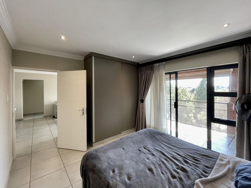 A well-lit bedroom featuring built-in wardrobes, tiled flooring, and direct access to a private balcony through sliding glass doors.