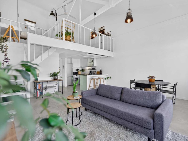 Open-plan living area featuring a mezzanine level, modern kitchen cabinetry, tiled flooring, and high ceilings with industrial-style pendant lighting.