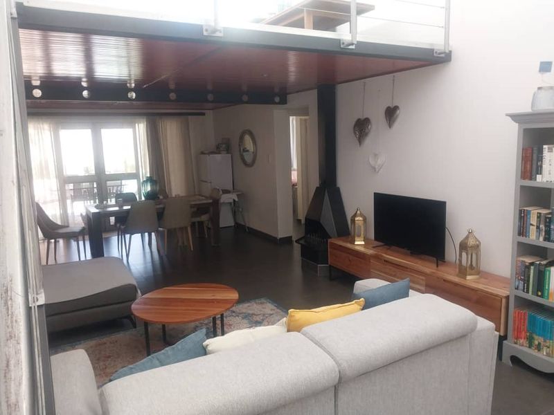 Spacious open-plan living and dining area featuring a modern freestanding fireplace, tiled floors, and a mezzanine level with metal railings.