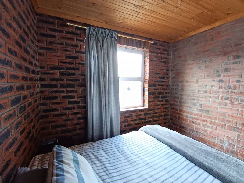 A bedroom featuring rustic exposed brick walls and a warm timber-clad ceiling, creating a cozy and textured living space.
